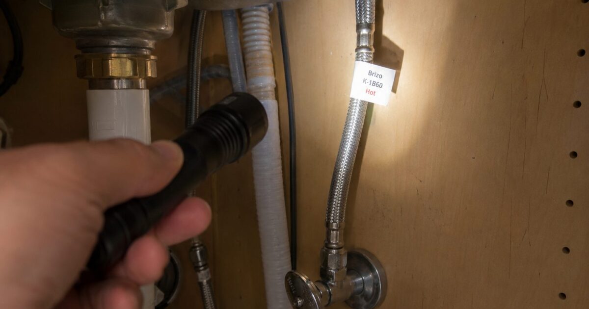 How to identify faucet brand — under-sink view showing braided supply lines where Delta and some Moen faucets keep their model tag