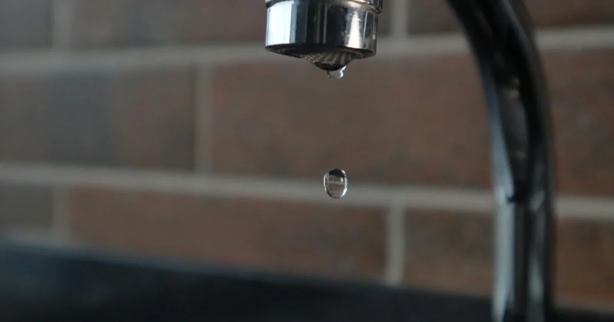 Faucet repair guide hero — kitchen faucet caught mid-drip with a water droplet falling toward the basin