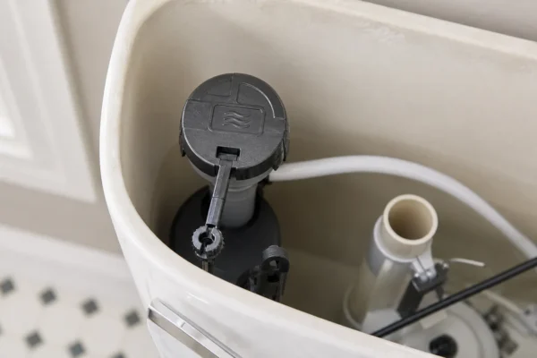 How to identify your toilet fill valve: homeowner reading the molded brand name on a fill valve's top cap inside an open toilet tank