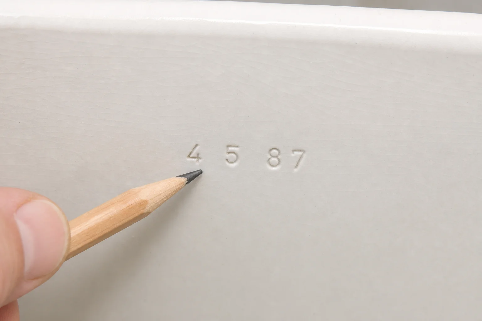 Close-up of a manufacture date stamp pressed into toilet tank porcelain, near the model number