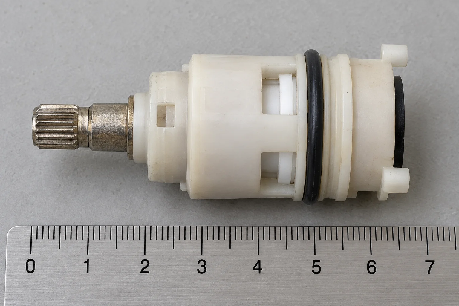 A ceramic faucet cartridge photographed from the side, showing its length and the base with locating tabs